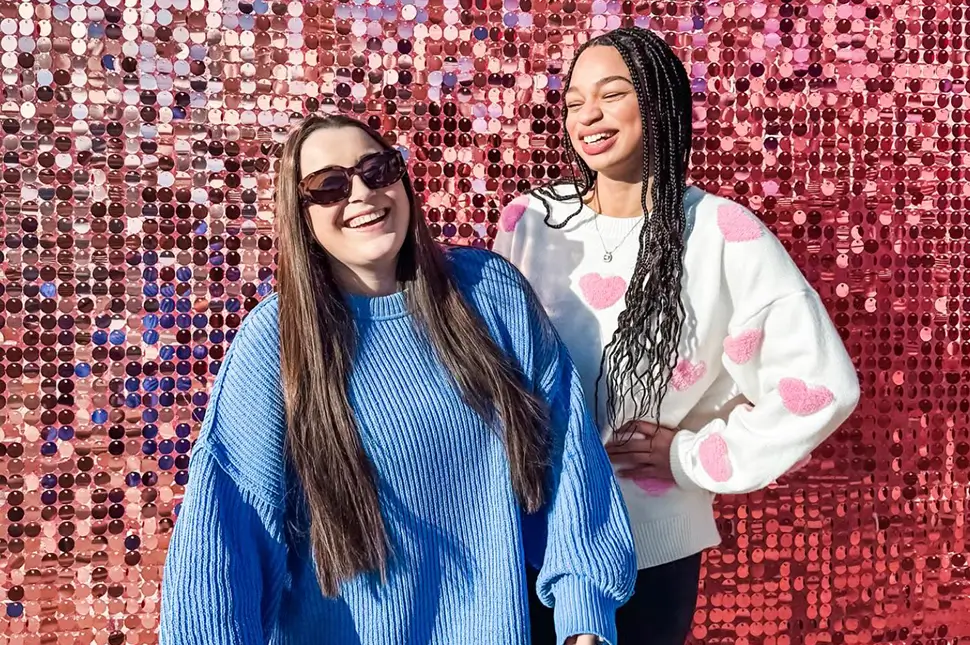 two young women standing in front of a sequin back drop